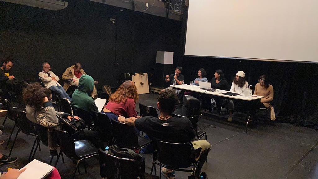Foto colorida mostrando os estudantes da SP Escola de Teatro na mesa "Território Siará" e o público sentado nas cadeiras da sala da sede Roosevelt