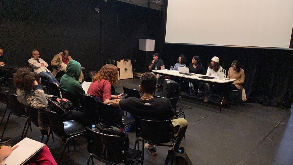 Foto colorida mostrando os estudantes da SP Escola de Teatro na mesa "Território Siará" e o público sentado nas cadeiras da sala da sede Roosevelt