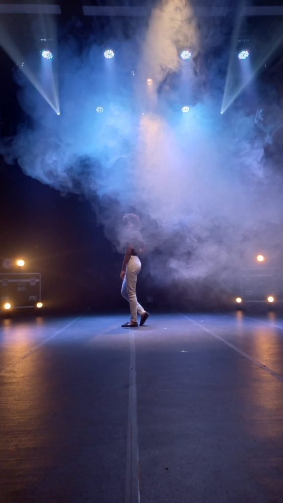 Foto com uma pessoa no palco sob o efeito de fumaça