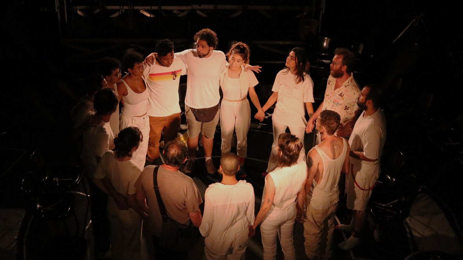 Foto colorida com estudantes da SP Escola de Teatro em uma roda encenando no experimento cênico