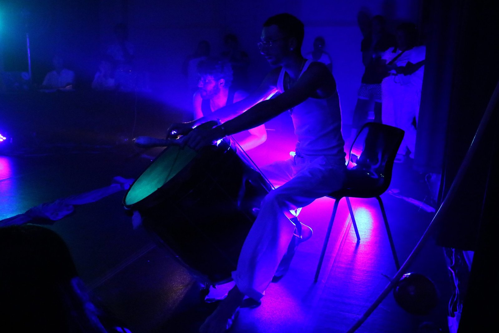 Foto colorida com luz azul mostrando um estudante da SP Escola de Teatro tocando um instrumento de percussão em experimento cênico