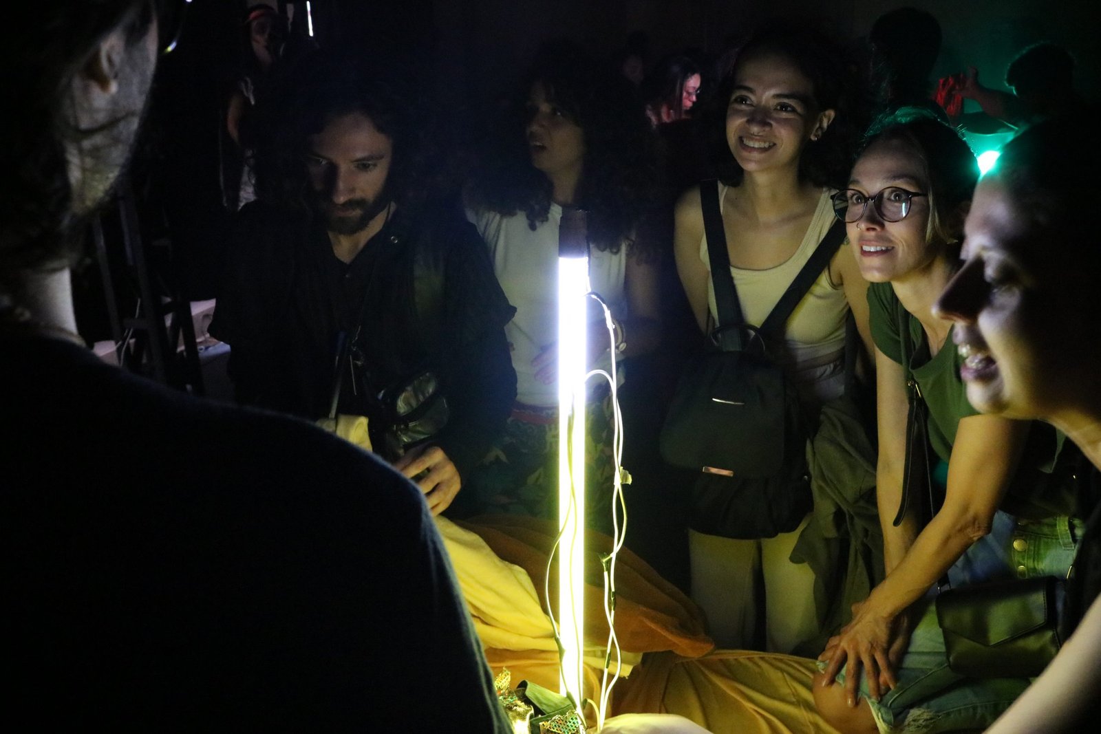 Foto colorida mostrando algumas pessoas vendo uma luz ligada em experimento cênico