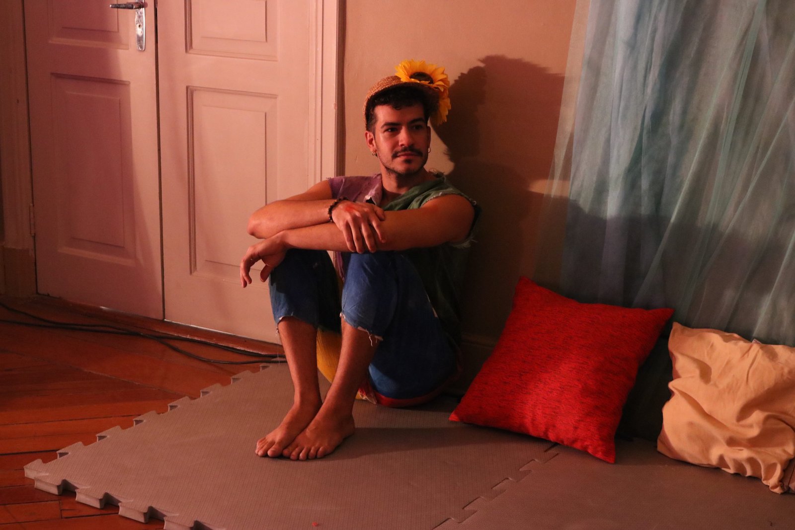 Foto colorida mostrando um estudante da SP Escola de Teatro sentado no chão com os braços apoiados nos joelhos em experimento cênico