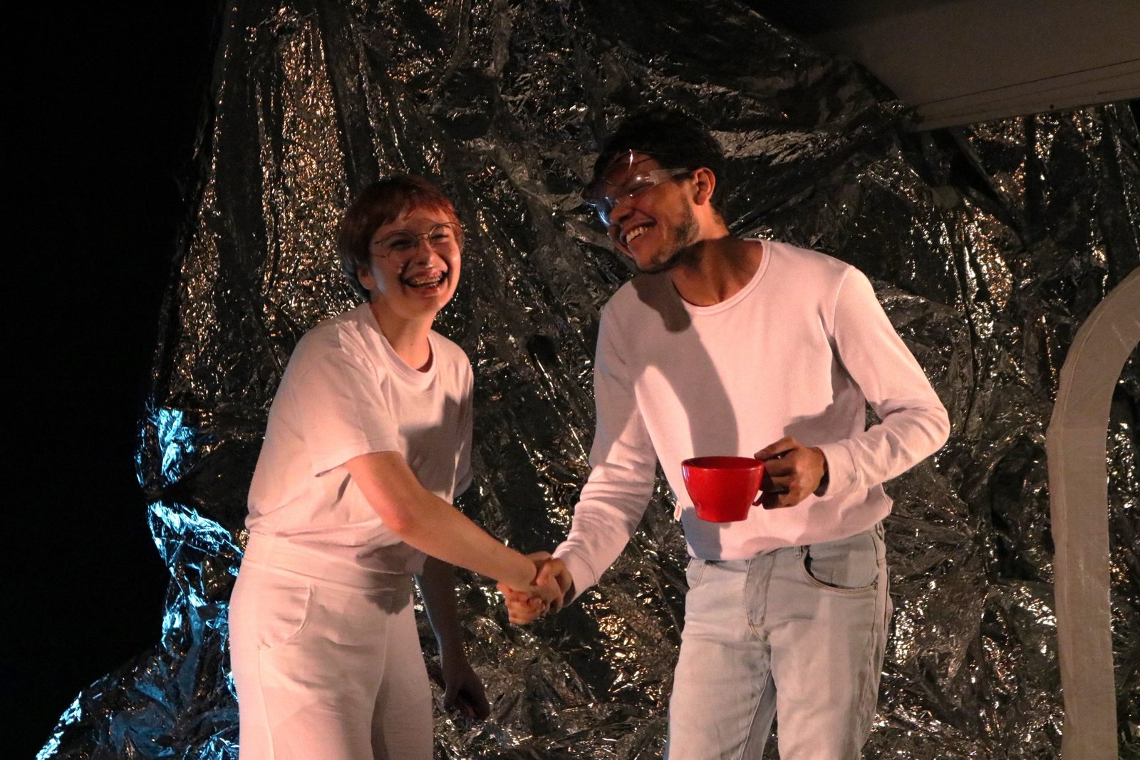 Foto colorida mostrando dois estudantes da SP Escola de Teatro se dando às mãos em experimento cênico