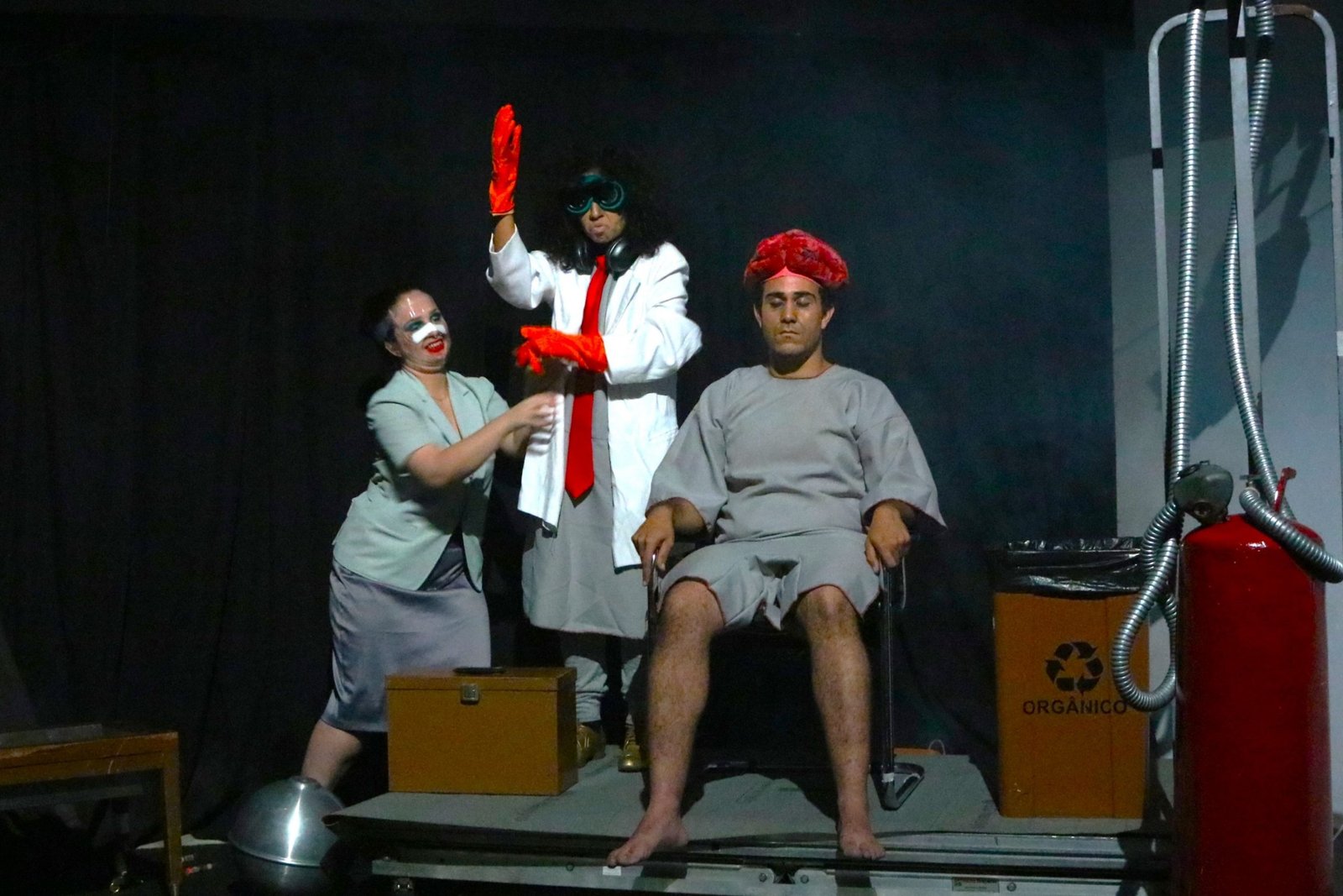 Foto colorida mostrando três estudantes da SP Escola de Teatro em experimento cênico