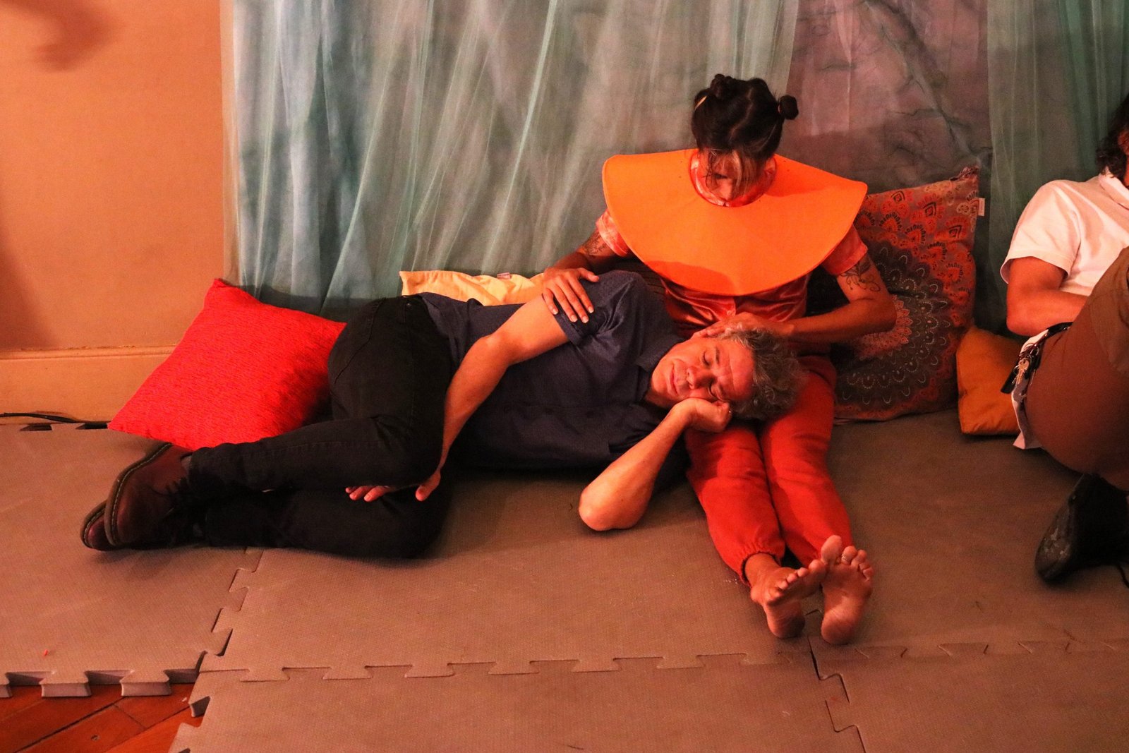 Foto colorida mostrando dois estudantes da SP Escola de Teatro, um sentado no chão e outro deitado no colo, experimento cênico