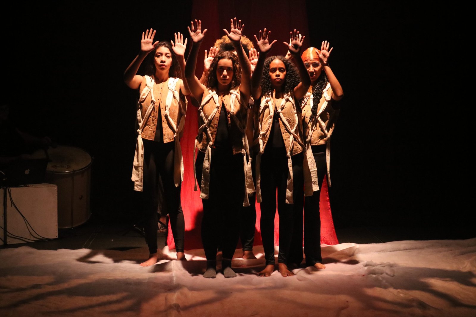 Foto colorida mostrando estudantes da SP Escola de Teatro com as mãos para cima em experimento cênico
