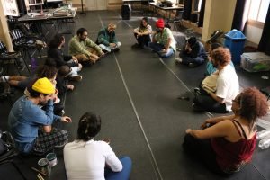 Fotografia colorida mostra turma de sonoplastia sentada em círculo com Barulho Max