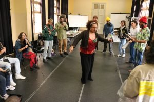Fotografia colorida mostra Tâmara David regendo a turma em aula com Barulho Max