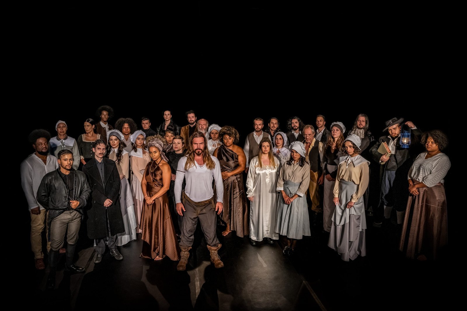 Imagem colorida de pessoas no palco, na peça As Bruxas de Salém